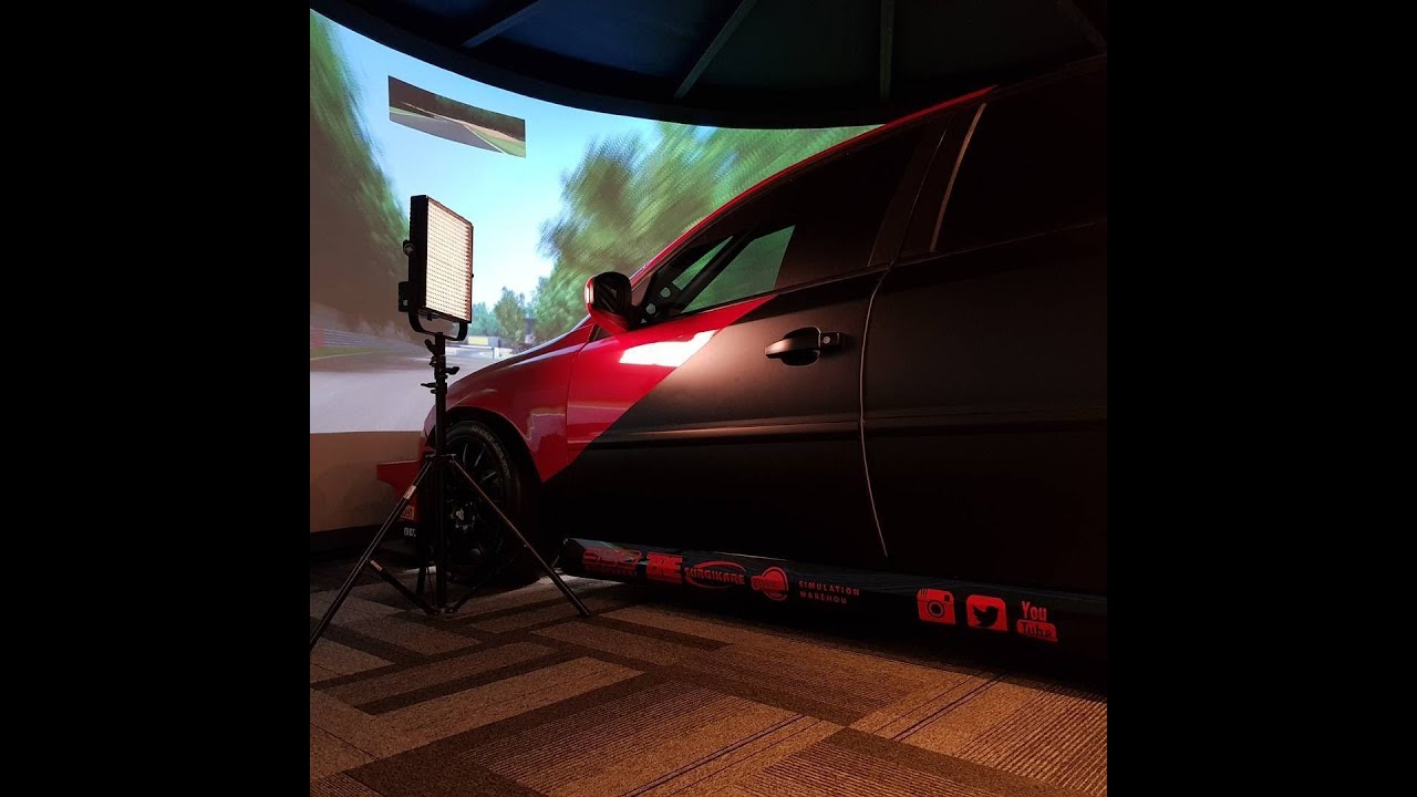 The red GTS RS full-car simulator beside the curved projection screen, from the 2021 studio film